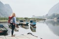 Caucasian blonde woman with backpack stands on boat pier in Muang Ngoi village, Laos