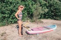 Caucasian blonde woman inflates sup surfboard with pump on beach.