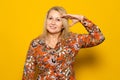 Caucasian blonde woman in a patterned dress doing the military salute isolated over yellow background, fulfilling the Royalty Free Stock Photo