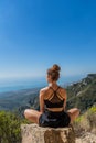 Caucasian blonde woman sitting on a rock in the mountain with her legs crossed and looking at the landscape with a straight back