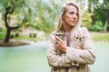 Caucasian blonde woman walk in green park on sunny summer or spring day with cup of hot beverage.