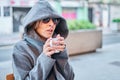Caucasian blonde woman wearing sunglasses and coat hoodie sitting in a bar terrace having a cup of coffee Royalty Free Stock Photo