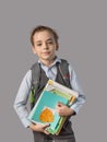 Caucasian boy with a backpack for books and a stack of textbooks in his hands on a gray background. Royalty Free Stock Photo