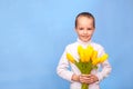 Caucasian boy dressed in white jacket holds a bouquet of yellow tulip and looks at the camera. Cute little babe smiling standing Royalty Free Stock Photo