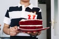 Caucasian boy holding a plate of a red velvet cake with red candles with flame