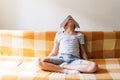 Caucasian boy sitting on couch covered his head with a notebook from fatigue