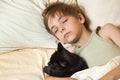 Caucasian boy  sleeps in bed hugging his beloved pet black cat Royalty Free Stock Photo
