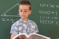 Caucasian boy standing at chalkboard in classroom holding schoolbook during maths lesson