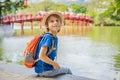 Caucasian boy tourist on background of Red Bridge in public park garden with trees and reflection in the middle of Hoan Royalty Free Stock Photo