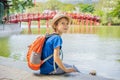 Caucasian boy tourist on background of Red Bridge in public park garden with trees and reflection in the middle of Hoan Royalty Free Stock Photo