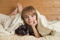 Caucasian boy  wakes up in the morning in bed hugging his beloved pet black cat. Friends covered with a blanket with Royalty Free Stock Photo