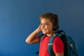 Caucasian boy wearing headphones with backpack standing on blue background, copy space Royalty Free Stock Photo