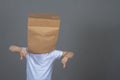 A Caucasian boy in a white T-shirt with a paper bag on his head shows a dislike gesture