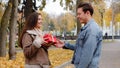 Caucasian boyfriend give red box small gift with gold ribbon to lovely pretty girlfriend young woman in autumn park