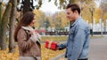 Caucasian boyfriend give red box small gift with gold ribbon to lovely pretty girlfriend young woman in autumn park