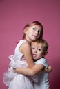 Caucasian brother and sister ,hugging on camera on pink background studio shot.