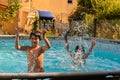 Caucasian brother and sister play splashing in pool in their backyard.