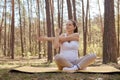 Caucasian brown haired pregnant woman wearing sportswear doing yoga in nature outdoors stretching her arms warming up looking away Royalty Free Stock Photo