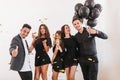 Caucasian brunette man in stylish shirt holding party balloons and glass of wine. Indoor photo of tired but happy