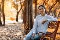 Caucasian brunette woman sitting on bench in natural park in autumn