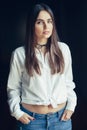 Caucasian brunette young beautiful girl woman model with long dark hair and brown eyes in white shirt tied in a knot, blue jeans Royalty Free Stock Photo