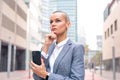 Caucasian business woman with pensive face using an app on her smartphone outdoors. Royalty Free Stock Photo