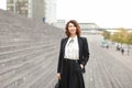 Caucasian businesslady standing on stairs outside in high buildings background.