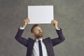 Caucasian businessman holding a blank white sheet of paper over his head on a gray studio background Royalty Free Stock Photo