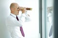 caucasian businessman spying using telescope thru office window