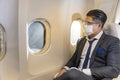 Caucasian businessman travels in formal wear with facial mask sitting comfortably in the aircraft with business class window seat Royalty Free Stock Photo