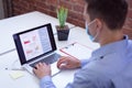 Caucasian businessman wearing face mask sitting at desk in office using laptop Royalty Free Stock Photo