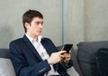 caucasian businessman working with tablet, wear suit, sitting on sofa, looking space and grey wall background. Young man work