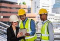 caucasian businesswoman in black suit wear helmet working on tablet with black engineer colleague. group of engineer working at