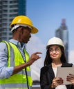 caucasian businesswoman with helmet in black suit happy working with tablet and looking at black engineer colleague at