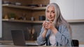 Caucasian businesswoman housewife senior freelancer mature lady sitting at home kitchen holds cup of tea or hot coffee Royalty Free Stock Photo