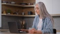 Caucasian businesswoman housewife senior freelancer mature lady sitting at home kitchen holds cup of tea or hot coffee Royalty Free Stock Photo