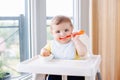 Caucasian child boy with dirty messy face sitting in high chair eating apple puree with spoon Royalty Free Stock Photo