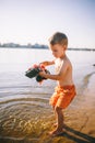 Caucasian child boy playing toy red tractor, excavator on a sandy beach by the river in red shorts at sunset day Royalty Free Stock Photo