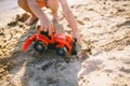 Caucasian child boy playing toy red tractor, excavator on a sandy beach by the river in red shorts at sunset day Royalty Free Stock Photo