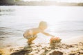 Caucasian child boy plays toy red tractor, excavator on sandy beach by the river in shorts at sunset day Royalty Free Stock Photo