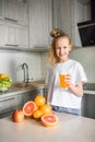 Caucasian child girl drinking orange juice indoors sitting at kitchen table. Kid healthy food nutrition concept. Royalty Free Stock Photo