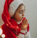 Caucasian child, lovely teenage girl in Santa hat, makes cherished wish and cute presents against the background of a light wall Royalty Free Stock Photo