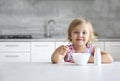 Caucasian child sitting at empty space table with bowl and spoon. Advertisement design. Little girl have a meal. Kid eating at Royalty Free Stock Photo