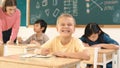 Caucasian child smiling at camera while doing classwork at classroom. Pedagogy. Royalty Free Stock Photo