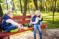 Caucasian children play chess on wooden chessboard in park bench. Brothers and sister big friendly active mental family spend time Royalty Free Stock Photo