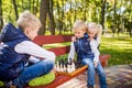 Caucasian children play chess on wooden chessboard in park bench. Brothers and sister big friendly active mental family spend time Royalty Free Stock Photo