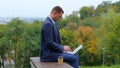 Caucasian classy man working on laptop typing on keyboard while sitting on bench in park with beautiful view. Side view Royalty Free Stock Photo