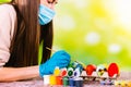 Caucasian concentrated girl in medical mask and disposable gloves decorates handmade eggs for the pascal holidays in