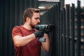 Construction man working with screwdriver on metal fence