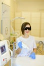 Caucasian cosmetologist wearing special purpose glasses and latex gloves sitting near permanent makeup device.